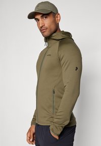 Olivengrønt zip-up hoodie med høj krave, justerbar hætte og sorte detaljer. Blød tekstur, tætsiddende design, inklusive lynlåslommer.