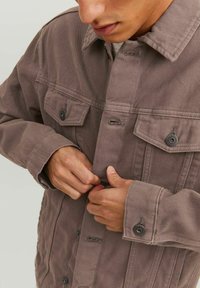 Giubbotto di velluto a coste marrone con grandi tasche sul petto, chiusure a bottone e colletto a punta; cuciture visibili e tessuto testurizzato.