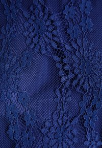 Tecido azul marinho com padrões de renda floral intrincados e uma sobreposição de malha texturizada, criando uma aparência detalhada e em camadas.