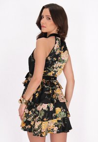 Schwarzes Blumenkleid mit einem gerafften Saum, verziert mit großen rosa und gelben Blumen. Der Halterneck-Stil verfügt über einen schlichten Rücken und einen taillierten Bindegurt.