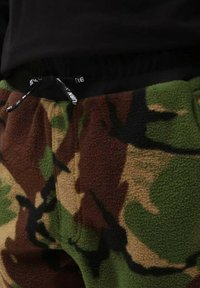 Pantalons de jogging en polaire avec un motif camouflage dans des teintes de vert, marron et beige. Comprend une taille élastique avec un cordon de serrage.