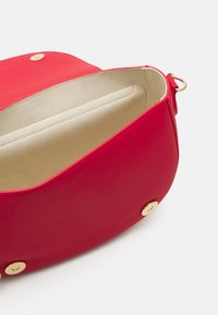 Červená kožená taška s hladkým povrchem a zlatým kováním. Interiér je béžový semiš s rozdělěným oddílem.