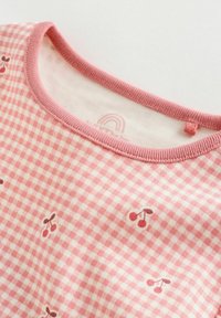 Rózsaszín és fehér kockás vászon, elszórt cseresznyemintákkal és rózsaszín bordázott nyakkivágással egy puha ruhadarabon.