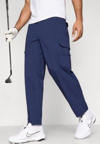 Pantalones cargo azul marino hechos de mezcla de algodón, con múltiples bolsillos, un ajuste relajado y diseño de pierna cónica, combinados con zapatos deportivos blancos.