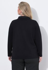 Haut noir à manches longues avec une texture douce et un col, associé à un pantalon rayé noir et blanc. Lignes épurées et coupe décontractée.