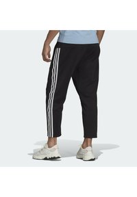 Joggers negros cortos con tres rayas verticales blancas a lo largo de los laterales, que presentan una cintura con cordón y un diseño de pierna ajustada.