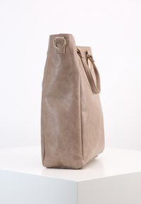 Bolso de mano de piel sintética beige con forma rectangular, base plana y herrajes en tono dorado; cuenta con una sola correa para el hombro.