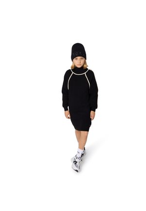 Black knitted dress with a high neck and white accent seams. Paired with a black beanie featuring a logo, white socks, and gray sneakers.
