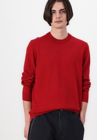 Red knit sweater with a crew neckline and long sleeves. Soft texture, relaxed fit, featuring rolled cuffs and a straight hem.