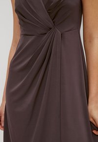 Robe mauve foncé avec un design drapé, des plis partant de la taille, une texture lisse et un décolleté en V.