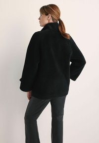 Czarna, puszysta kurtka polarowa z wysokim kołnierzem i luźnym krojem; ma obniżone ramiona i długie rękawy, w połączeniu z eleganckimi czarnymi skórzanymi spodniami.