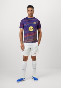 Barcelona fotbollströja i lila med vågiga, mångfärgade ränder, med en Spotify-logotyp; kombinerad med vita shorts, vita strumpor och blå fotbollsskor.