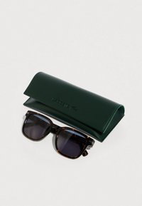 Tortoise shell rectangular sunglasses with dark lenses resting next to a dark green Lacoste branded leather case on white background.