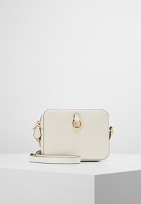 Piccolo borsa a tracolla rettangolare in pelle color crema con fibbia dorata e tracolla removibile, poggiata su una superficie bianca.
