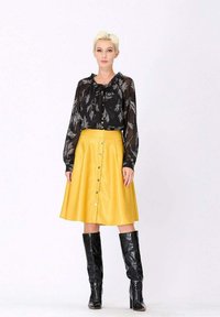 Blouse noire transparente avec motif de feuilles, col cravaté ; jupe jaune en A avec boutons à l'avant ; bottes noires brillantes jusqu'aux genoux.