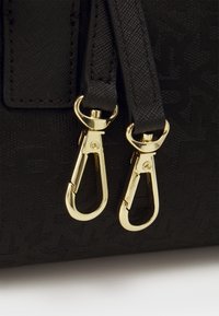 Bolso negro con herrajes en tono dorado, que incluye dos cierres de clip, y un material texturizado con un patrón en relieve.