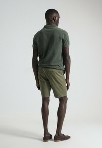 Polo de manga corta color verde olivo combinado con pantalones cortos verde olivo. La camisa tiene cuello y un diseño ajustado; los pantalones cortos son por encima de la rodilla y tienen bolsillos.