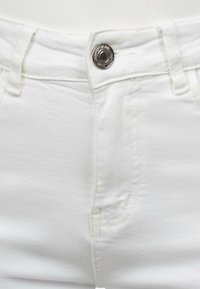 Des jeans en denim blanc en coton présentent une fermeture à bouton métallique, des passants de ceinture et des poches avant avec une finition texturée et de subtils détails de couture.