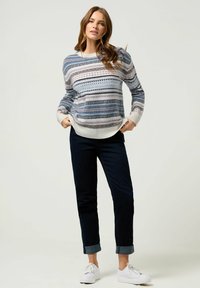 Sweter z dzianiny w paski w odcieniach niebieskiego, białego i szarego, z okrągłym dekoltem i ściągaczami przy rękawach. Zestawiony z ciemnymi, podwiniętymi dżinsami i białymi trampkami.