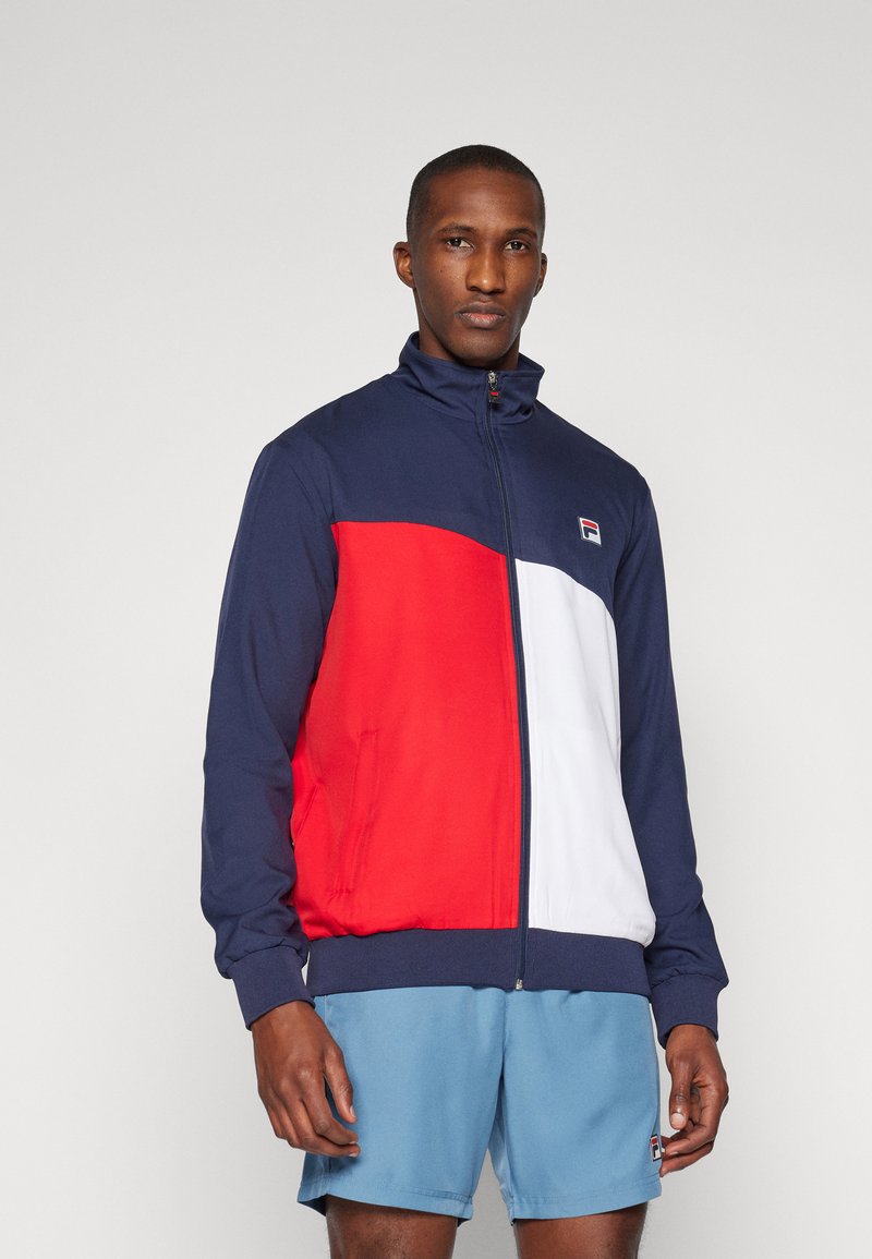 Men's zip-up track jacket in navy, red, and white. Features a high collar, side pockets, and ribbed cuffs. Made from smooth, lightweight fabric.