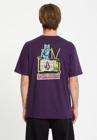 Lila Baumwoll-T-Shirt mit einem Grafikdruck eines Katers auf einem vintage Fernseher, verziert mit bunten Akzenten und dem Markennamen "VOLCOM" am unteren Rand.