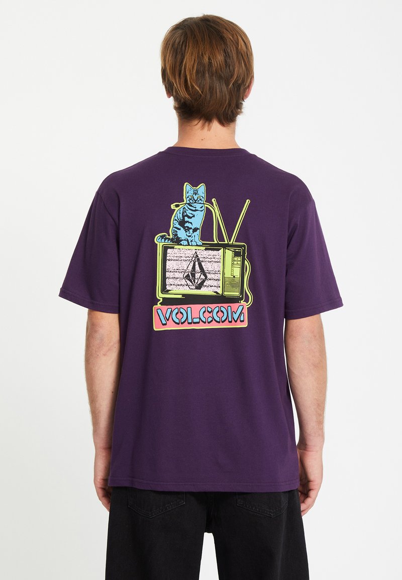 Paars katoenen t-shirt met een grafisch ontwerp van een kat op een vintage televisie, versierd met kleurrijke accenten en de merknaam "VOLCOM" aan de onderkant.