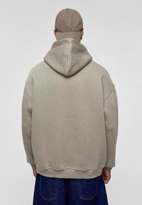 Beige hoodie met een ontspannen pasvorm, geribbelde manchetten en zoom. De stof heeft een soepele textuur, gecombineerd met donkerblauwe denim broeken.
