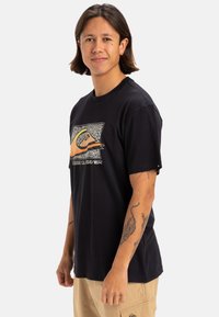 T-shirt in cotone nero con stampa grafica che presenta un'onda arancione e testo stilizzato. Maniche corte e scollatura rotonda. Tessuto leggero.