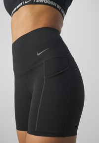 Gros plan d'une personne portant un short de sport Nike noir taille haute avec poche latérale et une brassière de sport Nike assortie.