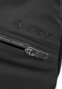 Tasca in tessuto nero con logo GORE-TEX, dotata di cerniera orizzontale e un'etichetta che indica "Tasca Riscaldante" vicino alla chiusura della zip.