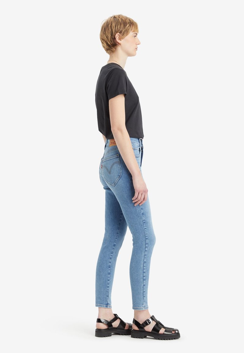 T-shirt noir à manches courtes, jeans skinny bleu clair et sandales noires à lanières avec semelles épaisses, vues de côté.