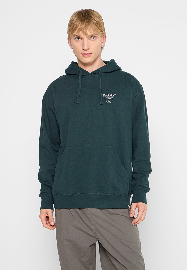 Mörkgrön hoodie i mjukt tyg, med en framficka, justerbar dragsko-huva och vit logotext på bröstet.