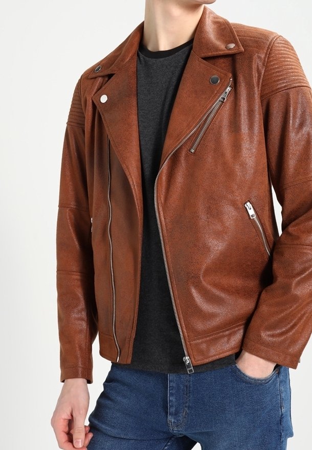 Giacca da motociclista in pelle marrone con chiusure a zip, dettagli testurizzati sulle spalle e vestibilità slim. Indossata sopra una maglia nera e jeans blu.