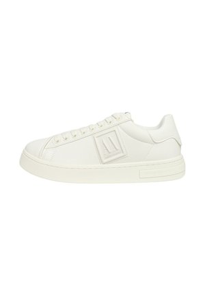 Zapatilla de cuero blanca con superficie texturizada, punta redonda, suela plana y diseño minimalista que presenta una placa con el logo en el costado.