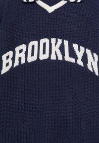 Námořnický pletený svetr s bílým textem "BROOKLYN". Má výstřih do V a pruhovaný límec. Texturovaná tkanina s žebrovaným vzorem.