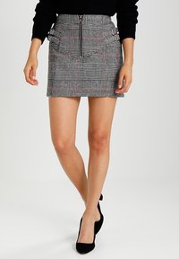 Rutigt mini kjol med en figurnära siluett, med en metallblixtlås fram och sidofickor, i svart, vitt och inslag av rött.