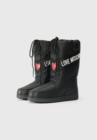 Svarta nylonankelstövlar med dragsko upptill, med vit "LOVE MOSCHINO" text och röda hjärtpunkter på sidorna. Platt gummisula.