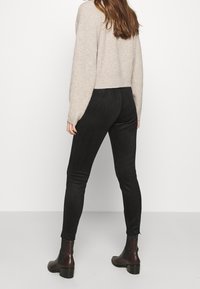 Czarne legginsy o dopasowanym kroju, miękka tkanina i gładka struktura, zestawione z beżowym swetrem z prążkowanej dzianiny i brązowymi botkami za kostkę.