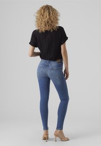 Štíhlé modré džíny s vysokým pasem, zadními kapsami a béžovou koženou nášivkou. V kombinaci s volným černým tričkem s krátkým rukávem a béžovými sandály.