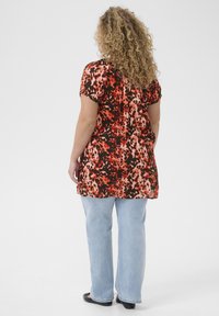 Haut à imprimé floral avec des manches courtes, présentant des couleurs rouge, orange et noire, associé à un jean en denim bleu clair et des chaussures noires.