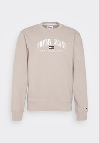 Beżowa bluza z okrągłym dekoltem, ściągaczami na rękawach i u dołu. Na przodzie logo „TOMMY JEANS NEW YORK CITY” w białym kolorze, z małym akcentem flagi.