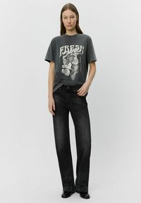 Maglietta grafica grigia con stampa bianca "FRESH" e jeans a gamba larga neri caratterizzati da un design strappato e brillanti spruzzate metalliche sui orli.