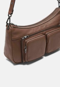 Bolso de hombro de cuero marrón con herrajes plateados, que cuenta con un compartimento principal con cremallera y dos bolsillos frontales con cremallera para mayor almacenamiento.