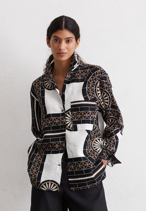 Zwart-witte gestreepte shirt met ronde motieven en geometrische ontwerpen, voorzien van een kraag en een borstzak. De stof lijkt licht van gewicht te zijn.