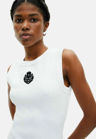 Canottiera bianca a costine con un design aderente, caratterizzata da un'emblema ricamato nero sul petto e ampi fori per le braccia per un look contemporaneo.