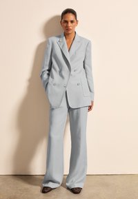 Blazer azul claro de doble botonadura con amplios solapas y bolsillos, combinado con pantalones de pierna ancha a juego. Zapatos negros texturizados de punta.