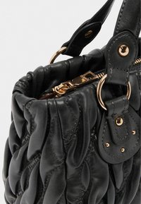 Borsa a tracolla in pelle trapuntata nera con chiusura a zip, accenti in oro e due manici corti per il trasporto. Dettagli superficiali testurizzati.