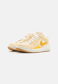 Nike sneakers featuring a smooth, light yellow leather upper, white laces, and a textured white midsole. Yellow accent logo and details.