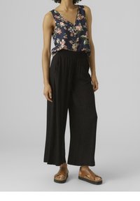 Květinová blůza s véčkovým výstřihem v námořnické modři, se růžovými a zelenými akcenty, spárovaná s černými širokými kalhotami. Hnědé sandály na platformě dokončují outfit.