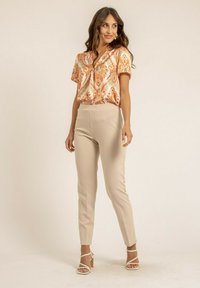 Blouse à manches courtes avec un motif cachemire orange et blanc, associée à un pantalon beige ajusté et des talons blancs à brides. Finition en tissu lisse.